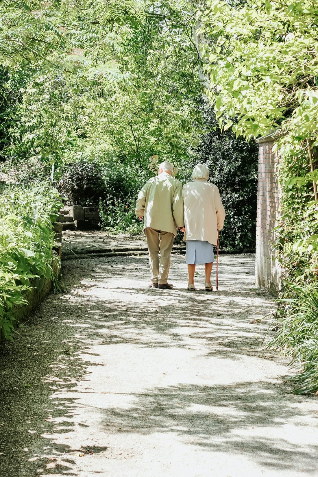 An older couple walking hand in hand along a green garden path